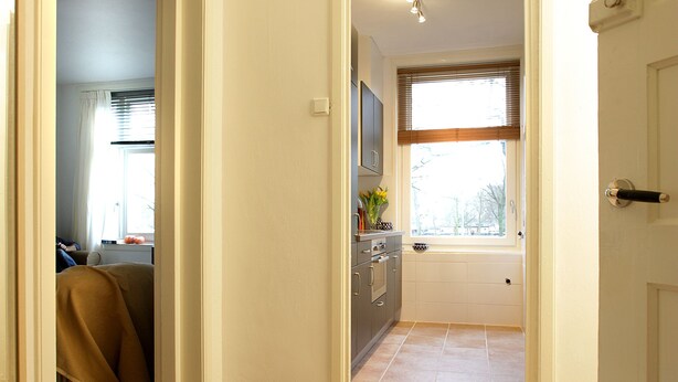 A hallway leading to a kitchen with a window, wooden flooring, and a door on the right. - Private Apartment in Good Area (Amsterdam)