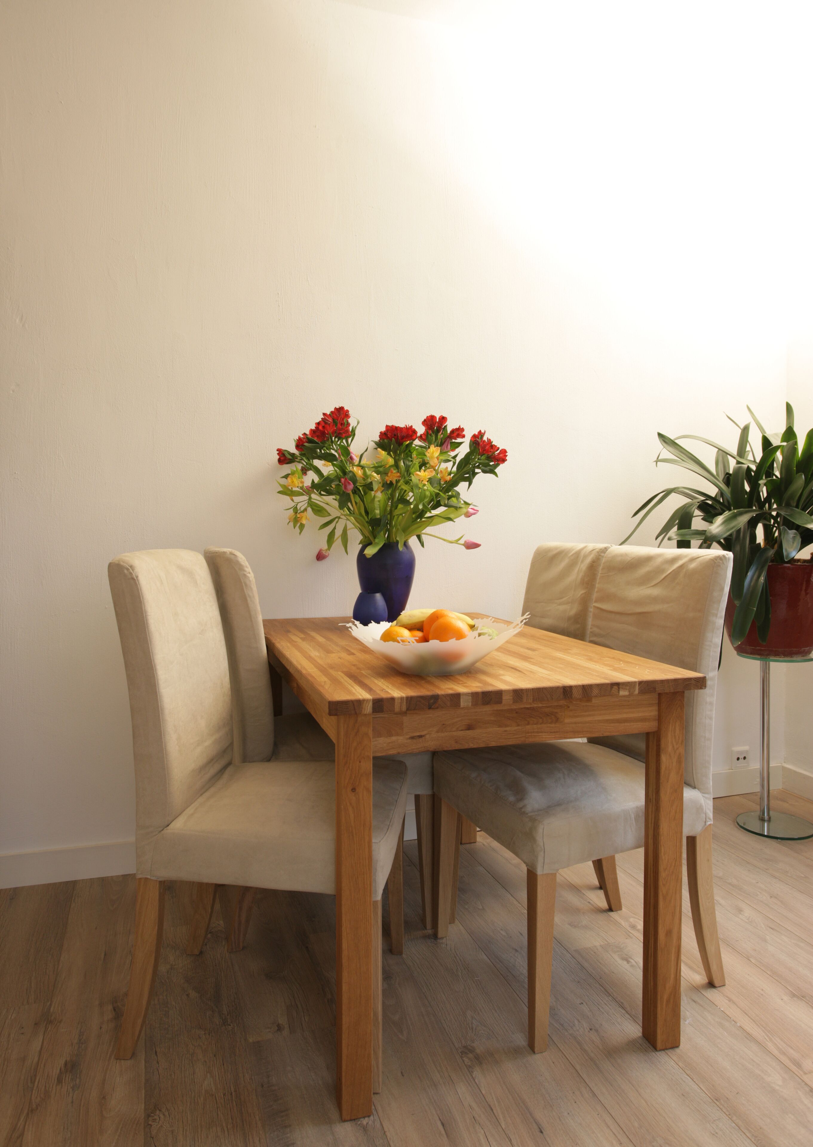 A wooden dining table with a vase of flowers and a bowl of fruit.