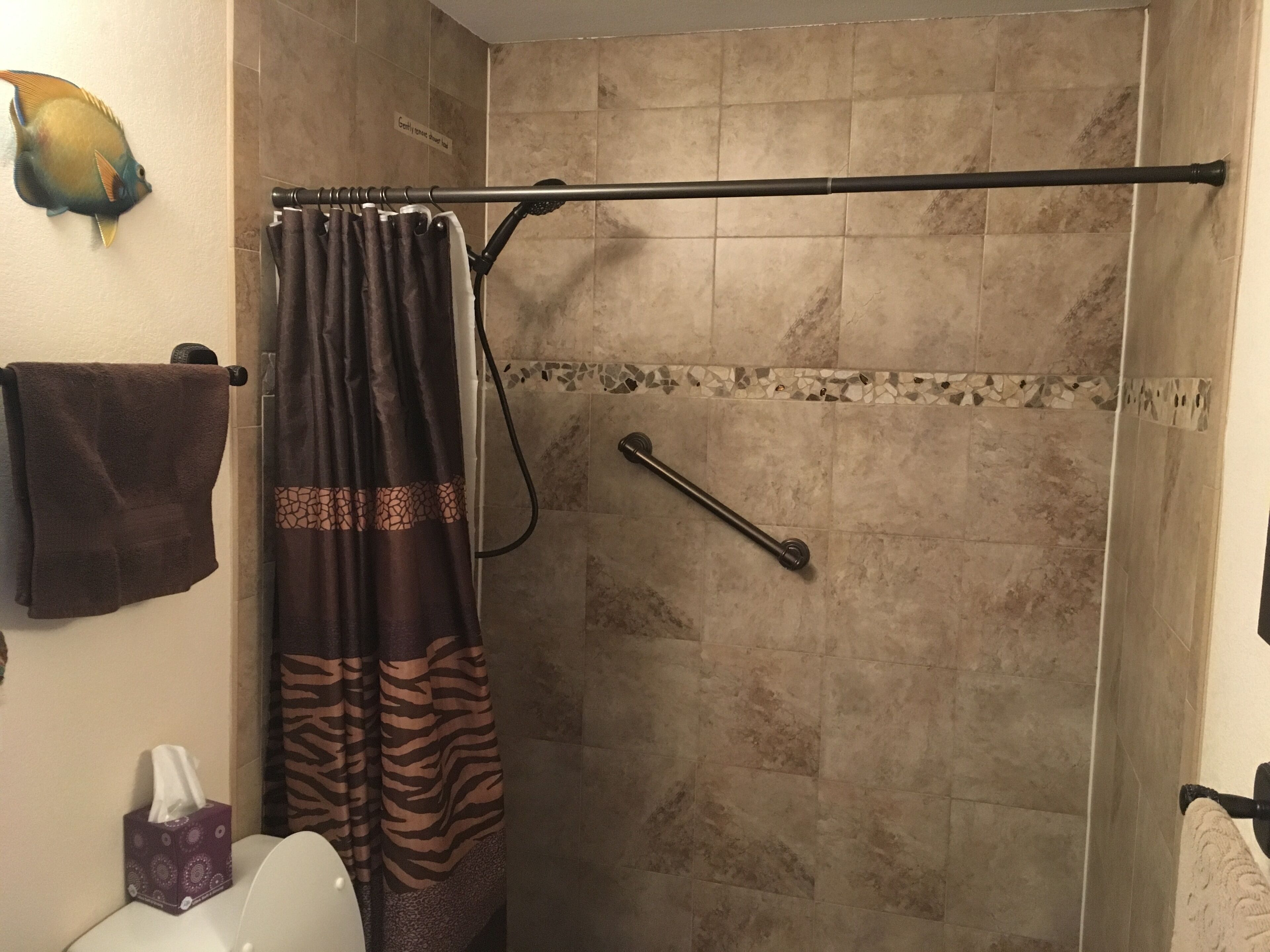 A shower with a zebra-patterned curtain, a towel rack with a brown towel, and a handrail.