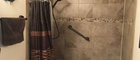 A shower with a zebra-patterned curtain, a towel rack with a brown towel, and a handrail.