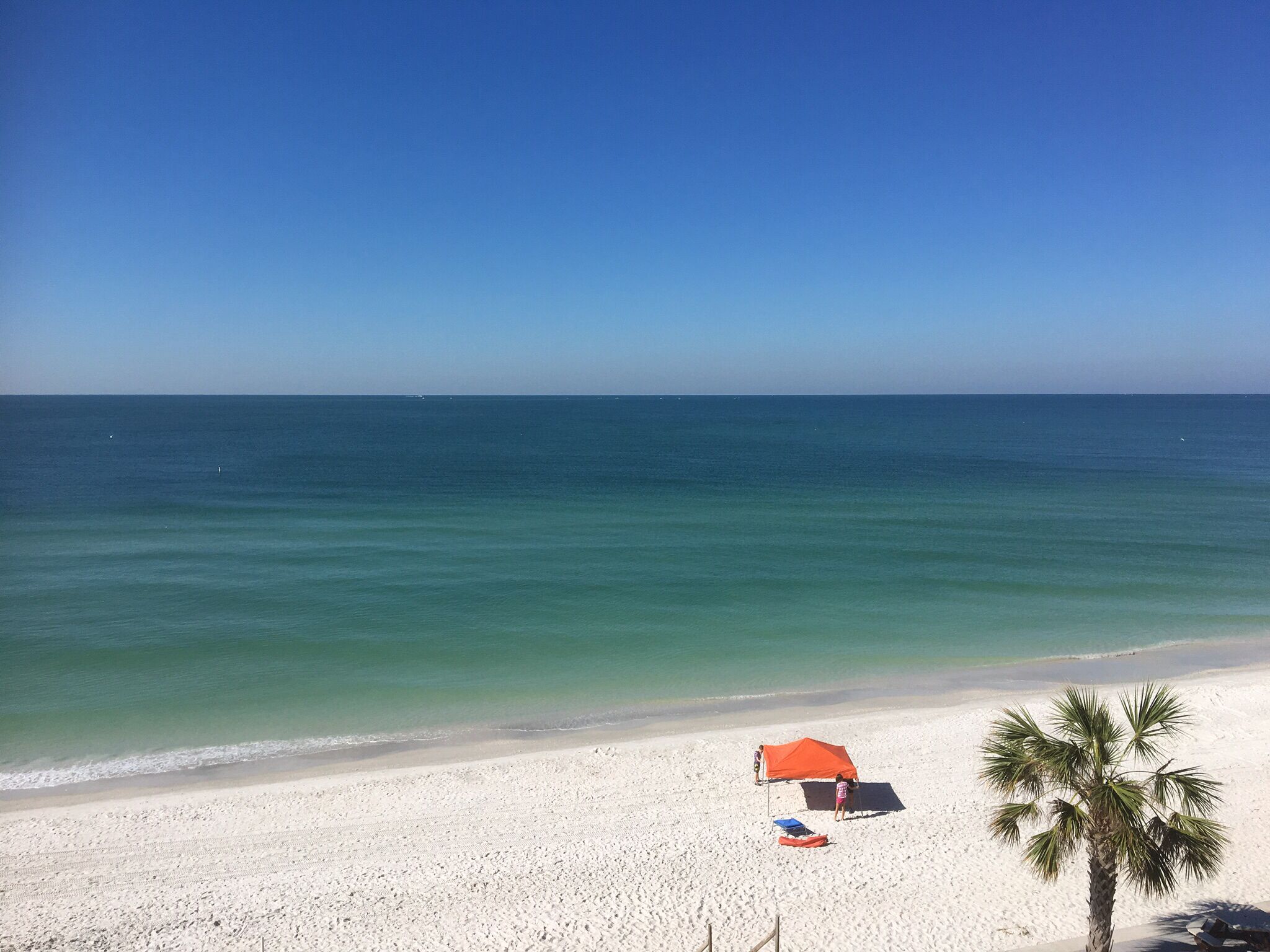 A beach with white sand, a clear blue sky, and calm ocean waters.