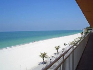 A beach view from a balcony with a railing, a sandy beach, and a clear blue sky.