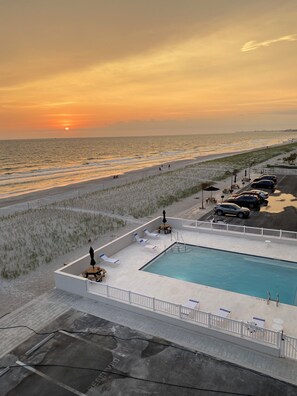 A pool area with lounge chairs and a view of the beach at sunset.