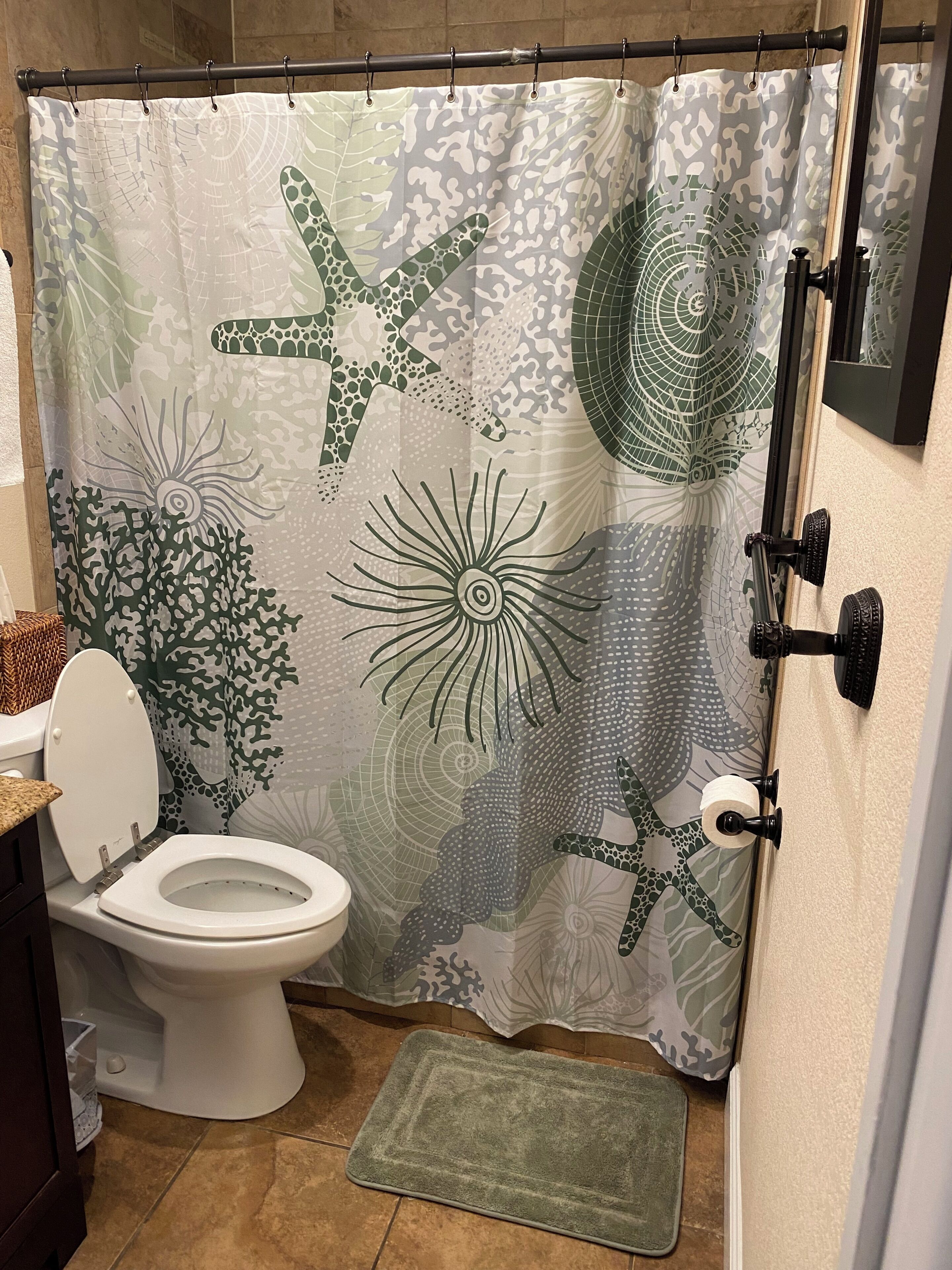 A bathroom with a toilet, a shower curtain with a marine life pattern, a towel rack, and a bath mat.