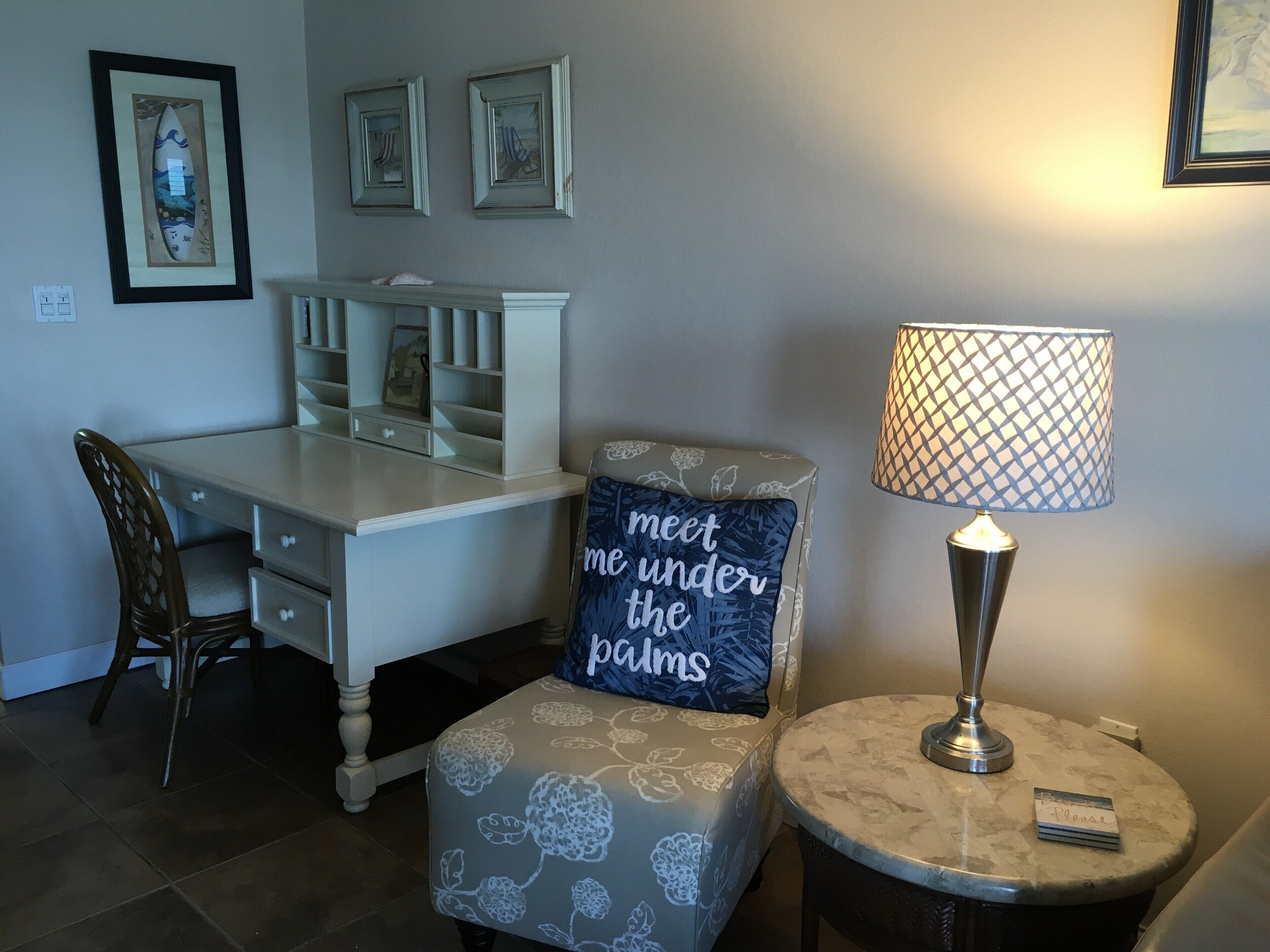A room with a desk, a chair, a lamp, and a small table.