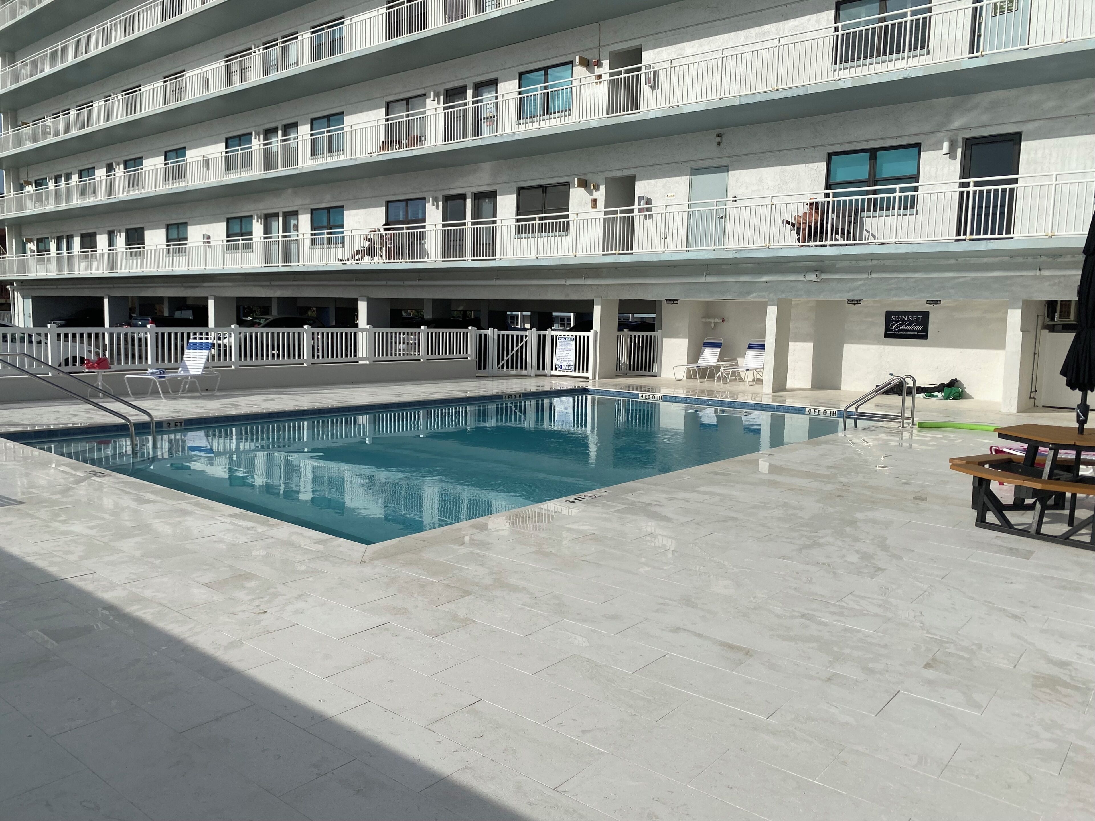 Un hotel de varios pisos con piscina, asientos exteriores y un letrero que indica una zona 'Sunset'.
