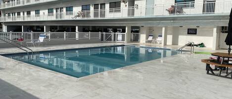 Un hotel de varios pisos con piscina, asientos exteriores y un letrero que indica una zona 'Sunset'.