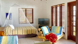 A spacious living area with a high ceiling, a bed with striped bedding, a sofa with colorful cushions, a television, and a glass-top coffee table with a vase of flowers. - Ti Zan: Views to Die For. Perfect for two (Gros Islet)