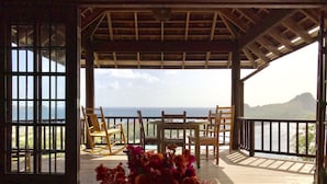 An open wooden deck with a table and chairs, a vase of flowers, and a view of the sea and mountains. - Ti Zan: Views to Die For. Perfect for two (Gros Islet)
