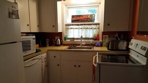 A kitchen with a microwave, sink, and stove. There's a window with a sign reading "The Mermaid Lounge".