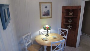 A dining area with a round wooden table, white chairs, a stained glass lamp, and a framed picture on the wall.