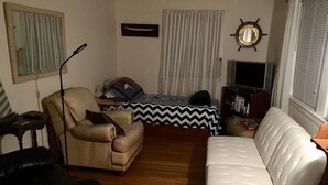 A living room with a sofa, armchair, and a bed with a chevron-patterned bedspread.