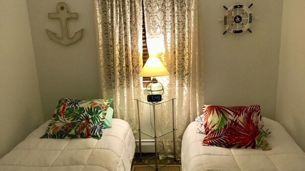 A room with two beds, a nightstand with a lamp, and nautical-themed decor.