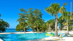 Zona de piscina con agua cristalina, rodeada de palmeras y vistas al océano.