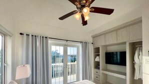 Habitación de hotel con cama, ventilador de techo, televisor, armario y balcón con cortinas.