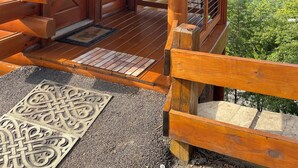 A log cabin with a wooden porch, a door with a 'No Smoking' sign, a window with a view of the forest, and a metal railing. - Couples Dream Getaway! Unobstructed Views of the Smoky Mountains National Park! (Sevierville)