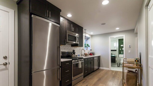 Una cocina moderna con electrodomésticos de acero inoxidable, armarios oscuros y suelo de madera.