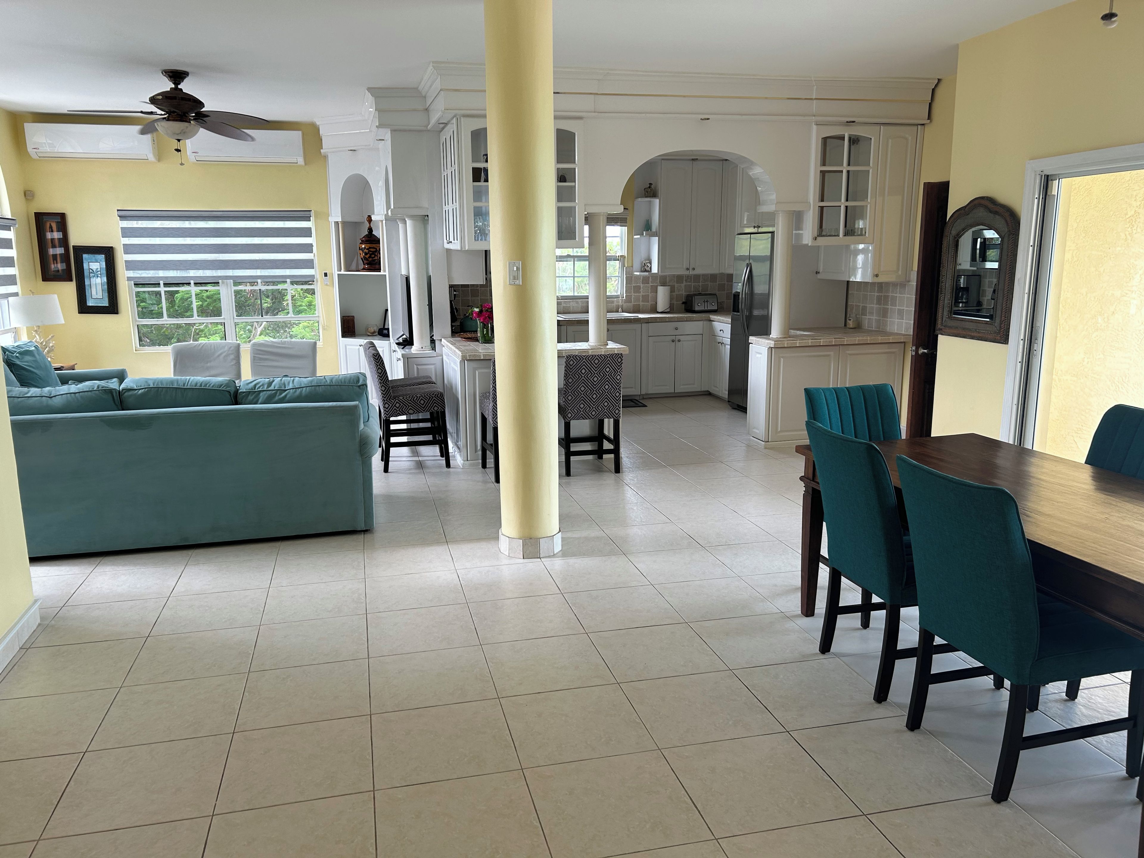 A spacious living area with a sofa, dining table, and chairs, connected to a kitchen with white cabinets and a tiled floor.