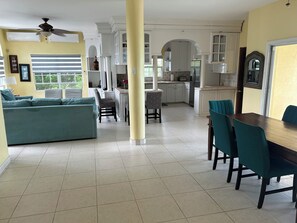 A spacious living area with a sofa, dining table, and chairs, connected to a kitchen with white cabinets and a tiled floor. - Luxury Turks & Caicos Villa with Infinity Pool on Chalk Sound (Providenciales)