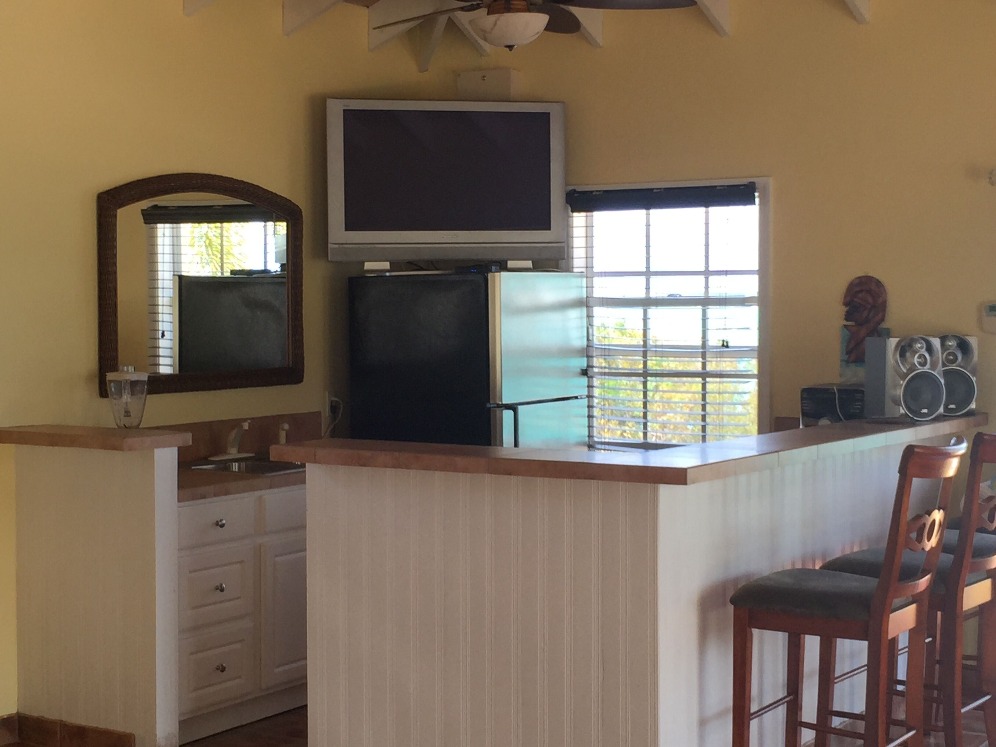 A compact kitchen with a refrigerator, a microwave, a sink, and a bar area with stools.
