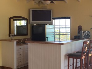 A compact kitchen with a refrigerator, a microwave, a sink, and a bar area with stools. - Luxury Turks & Caicos Villa with Infinity Pool on Chalk Sound (Providenciales)