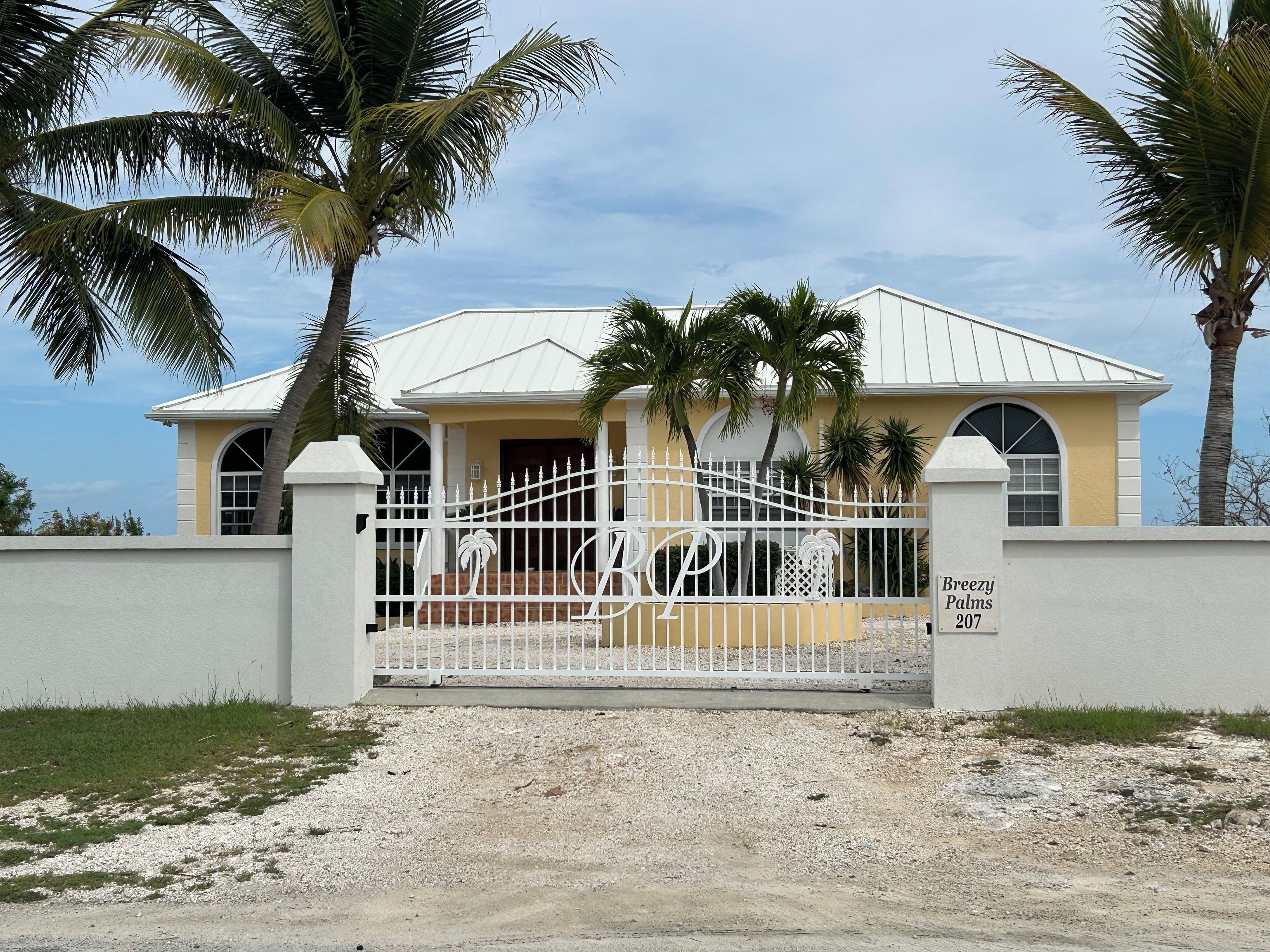 A gated property with a white metal fence, a palm tree, and a building with a yellow facade.