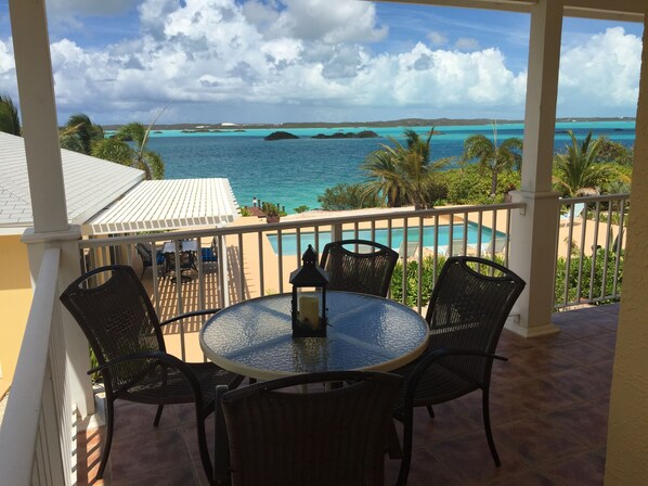 Een ronde tafel met stoelen op een balkon met uitzicht op een zwembad en turquoise water.