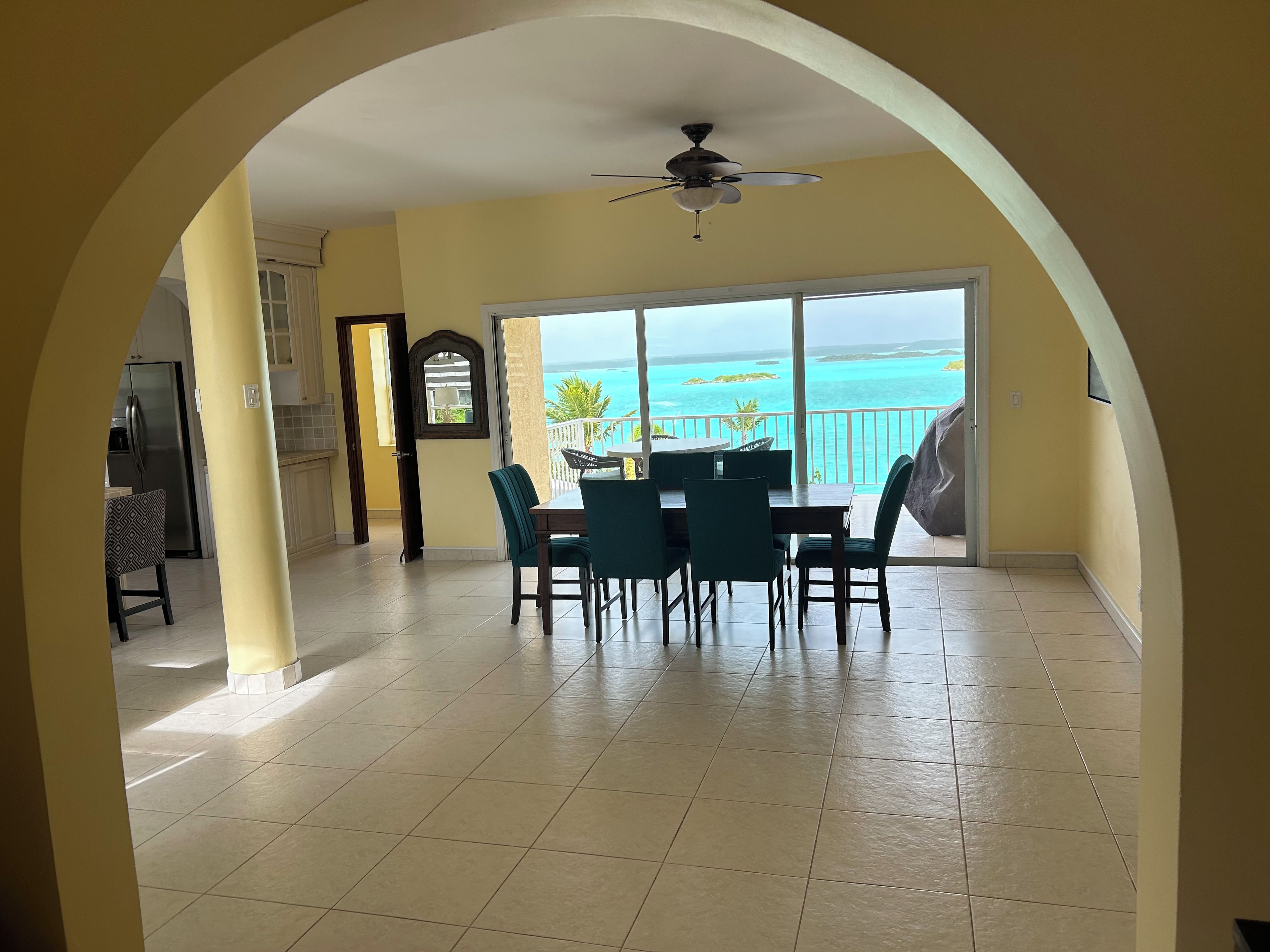 Zona pranzo con vista sull'oceano, una ventola a soffitto e una cucina sullo sfondo.