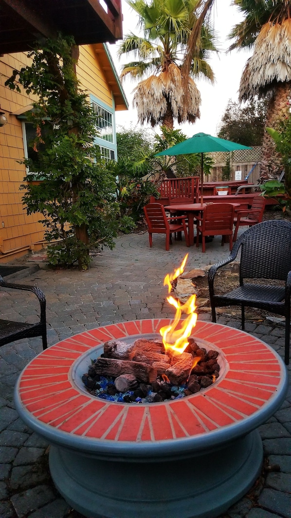 Un foyer circulaire où brûlent des bûches, entouré d’une terrasse en briques.