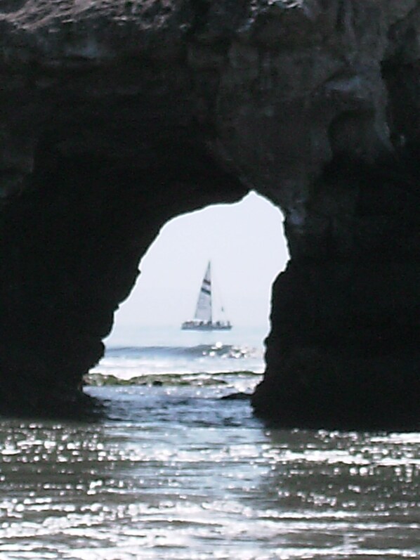 Vista a través de un arco rocoso, con un velero en la distancia.