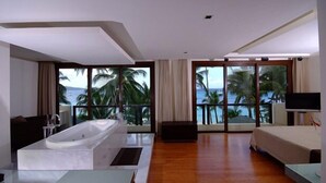 Una habitación de hotel moderna con una bañera grande, una cama, un televisor y un balcón con vistas a palmeras y al océano.
