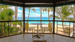 Una habitación con un amplio ventanal que da a una playa con palmeras y cielo despejado.
