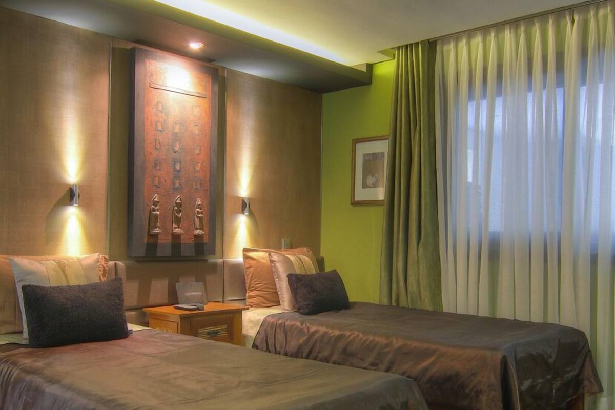 A hotel room with two beds, a wooden cabinet, and a green wall.