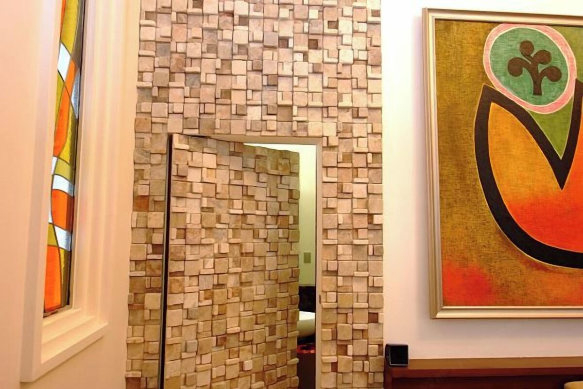 A room with a mosaic wall, a framed abstract painting, and a stained glass window.