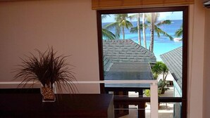 Una habitación con un amplio ventanal que da a una playa con palmeras y un cielo azul despejado.