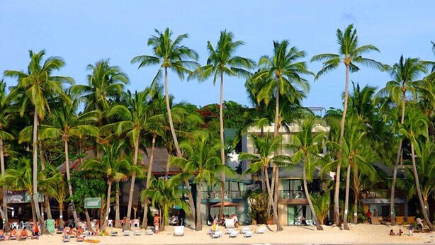 Una playa con palmeras, sillas de playa y un edificio con piscina.
