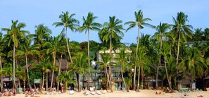 Una playa con palmeras, sillas de playa y un edificio con piscina.