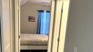 A bedroom with a single bed, a window with curtains, and a door leading to another room.