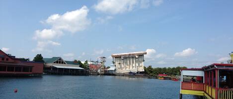 A waterfront hotel with a large building in the center, a dock with a yellow and red structure, and a calm blue sky.