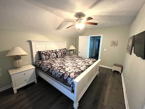 Een slaapkamer met een bed, nachtkastjes, een plafondventilator en een deur naar een andere kamer.