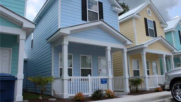 A row of two-story houses with a porch, white railings, and a small garden area.