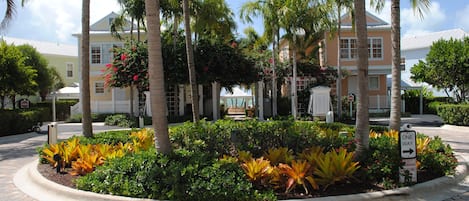 A landscaped area with palm trees, a one-way street sign, and a building with a white roof.