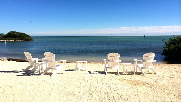 Una playa con sillas blancas y una vista despejada del océano.