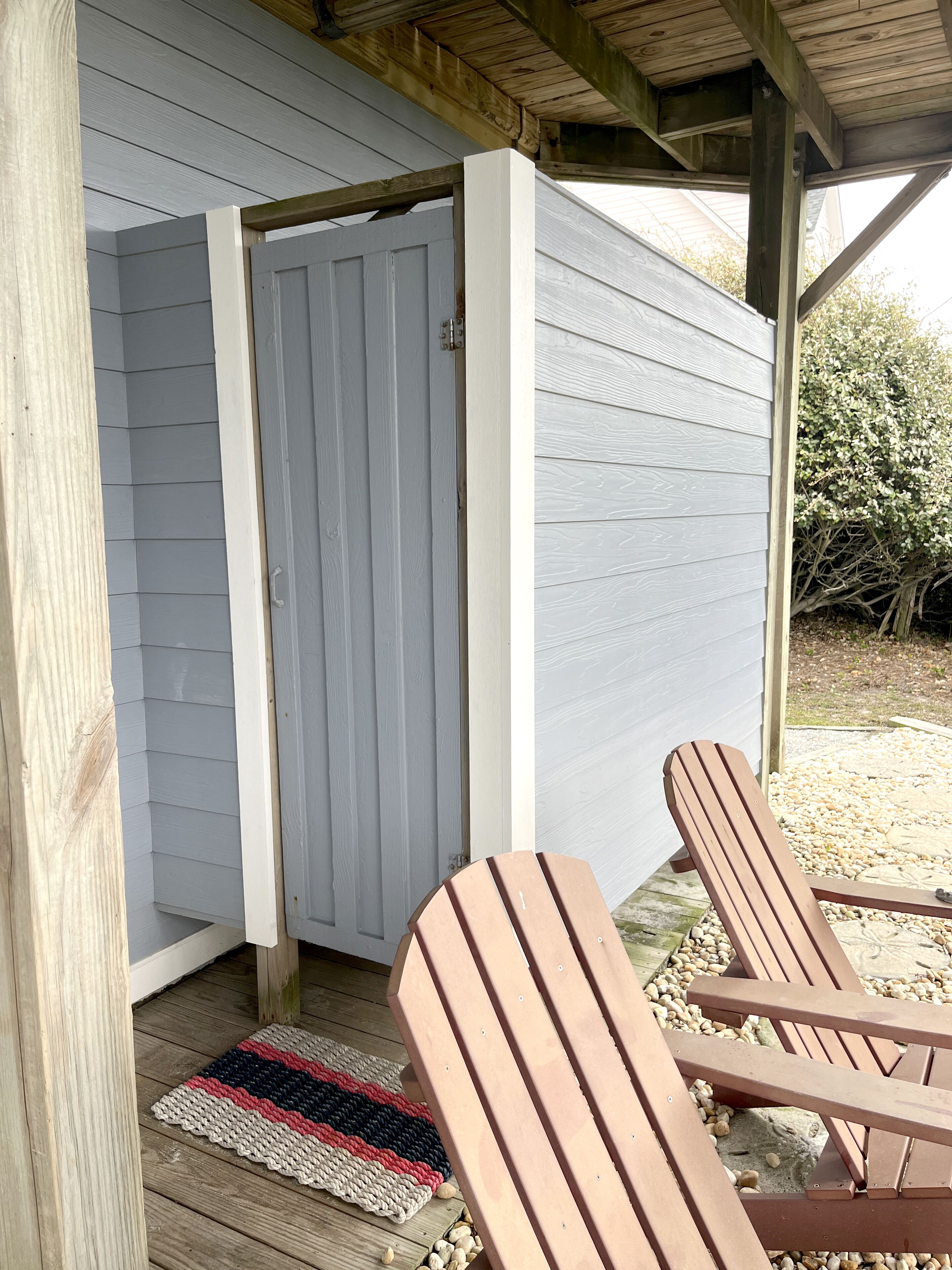 Une terrasse en bois avec deux fauteuils Adirondack, une porte en bois et un petit espace couvert doté d’un plafond en bois.