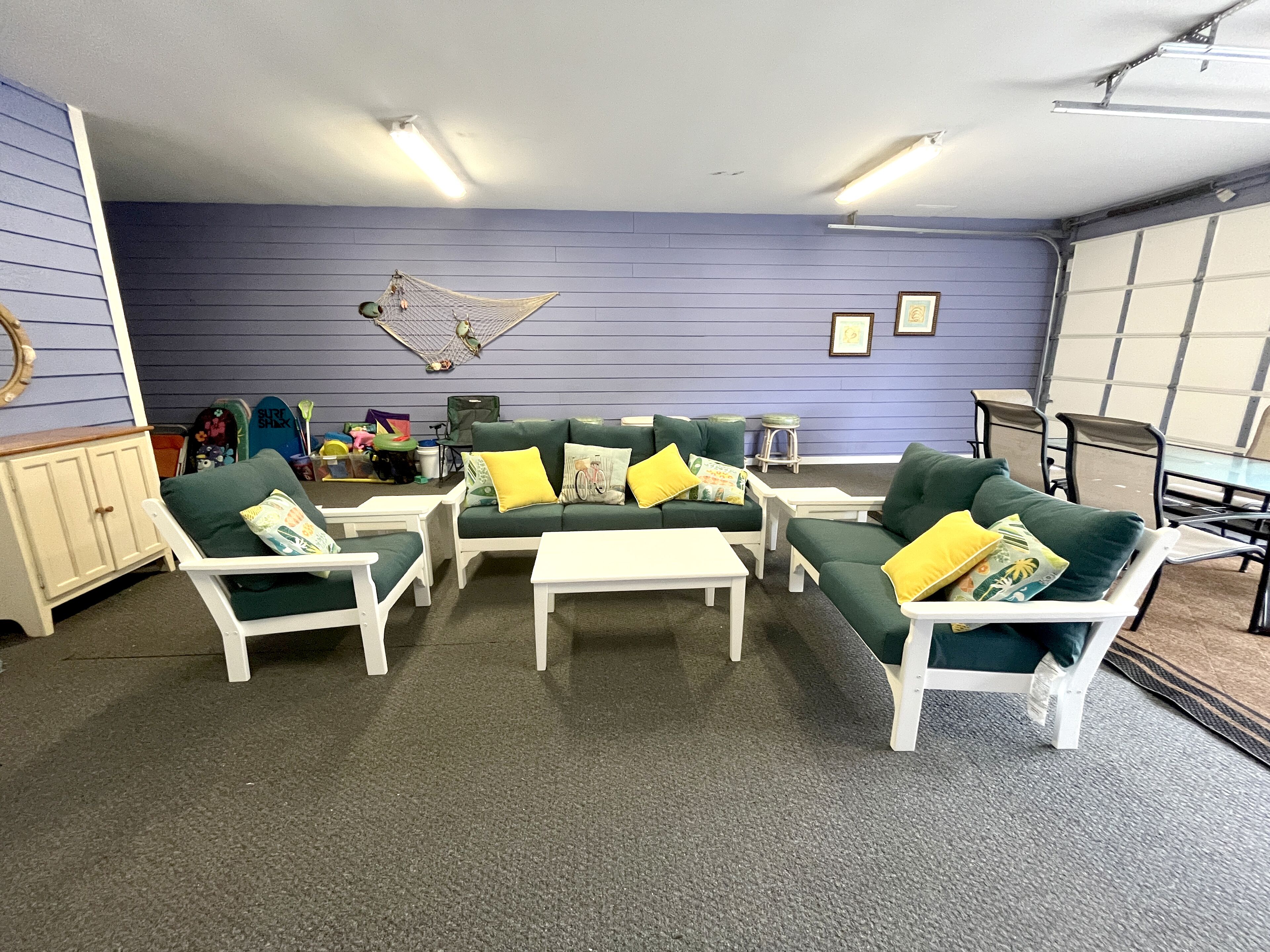 A room with a green sofa set, white armchairs, and a small table. There is a hammock, a cabinet, and a chair with toys.