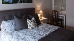 Un dormitorio con una cama, una mesita de noche, una silla, una ventana y un cuadro en la pared.