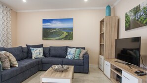 Una sala de estar con un sofá seccional, una mesa de centro, un televisor de pantalla plana y un cuadro de un paisaje.