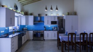 Una cocina con armarios blancos, salpicadero de azulejos azules, electrodomésticos de acero inoxidable y una zona de comedor con mesa y sillas.