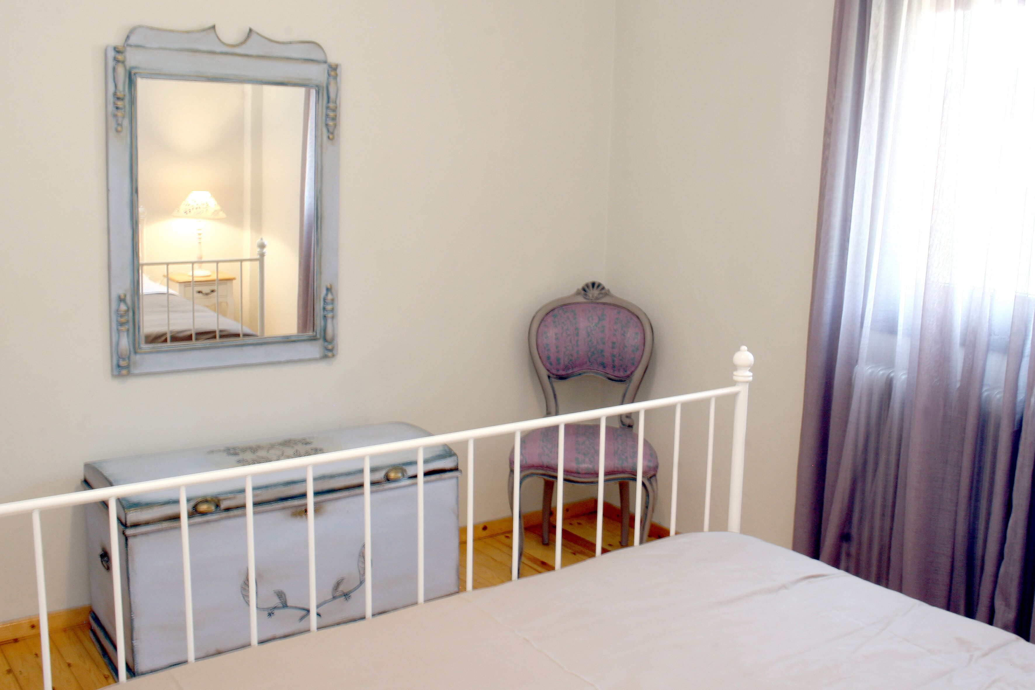 Un dormitorio con cama, cómoda, silla, espejo y ventana con cortinas.