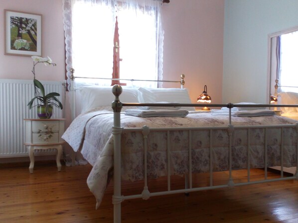 A bedroom with a four-poster bed, a bedside table with a lamp, a radiator, and a window with curtains.
